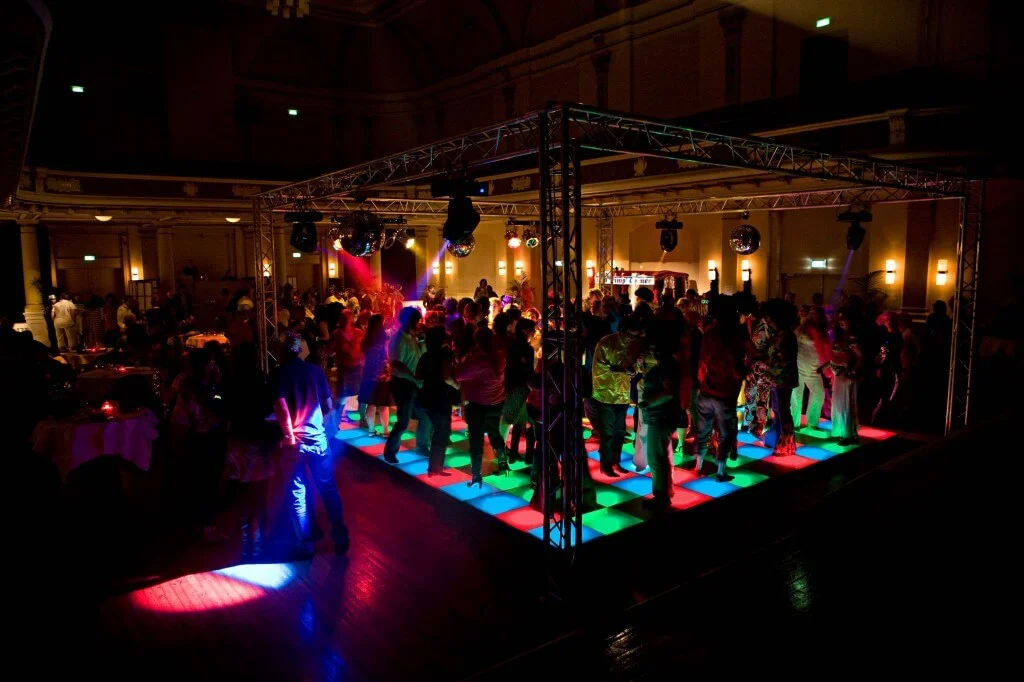 Mensen dansen op een verlichte dansvloer tijdens een feest in een grote zaal.