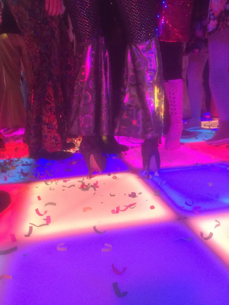 Dansvloer met kleurrijke verlichting en confetti onder de voeten van feestgangers.
