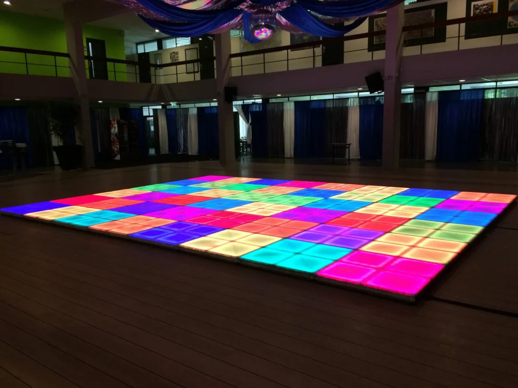 Kleurrijke verlichte dansvloer in een grote zaal met decoraties aan het plafond.