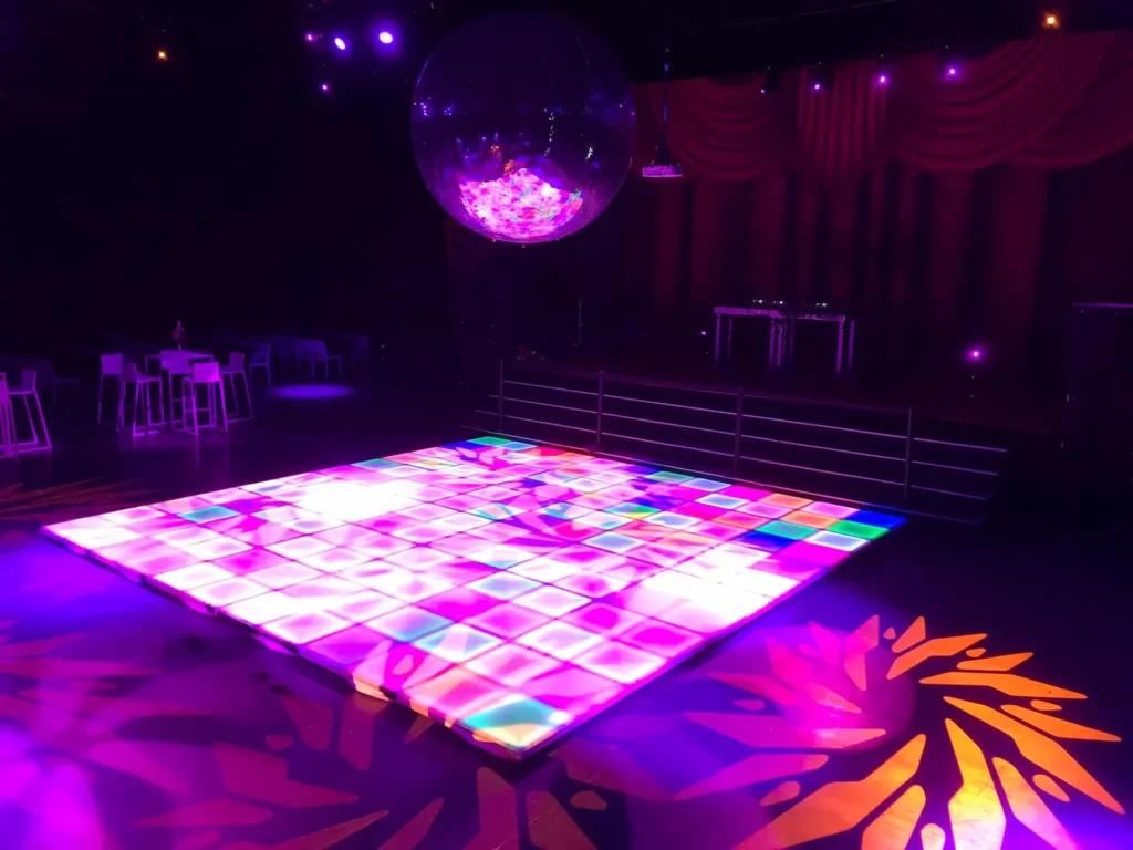 Een felverlichte dansvloer met kleurrijke patronen onder een grote discobal.